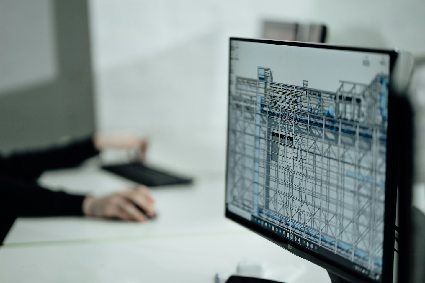 Na monitorze komputera wyświetla się trójwymiarowy model siatkowy, a dłonie spoczywają na klawiaturze.
